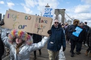 A young marcher hold signs that reads "NYC No Place for Hater" and another behind them "Stop Anti-Semitism" as they walk across the Brooklyn Bridge with the arch behind them