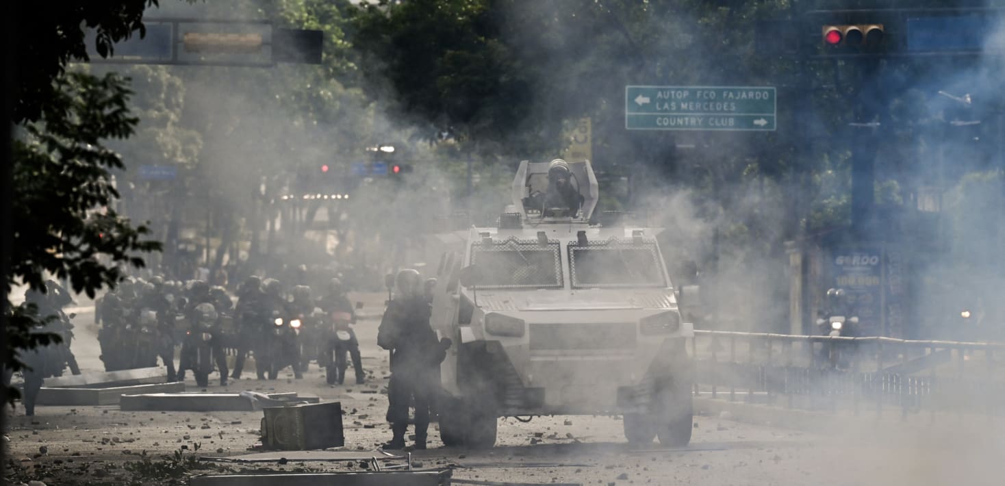 A tank on a dusty or smoky street with people in military garb.