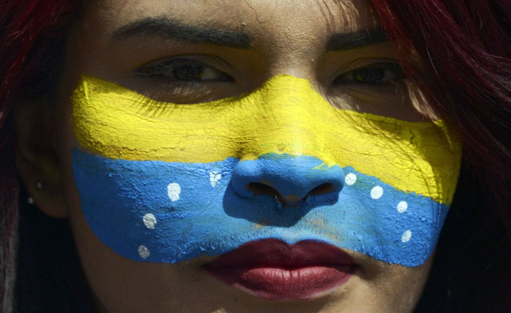 A woman with her face painted in the Venezuelan national flag's colors.